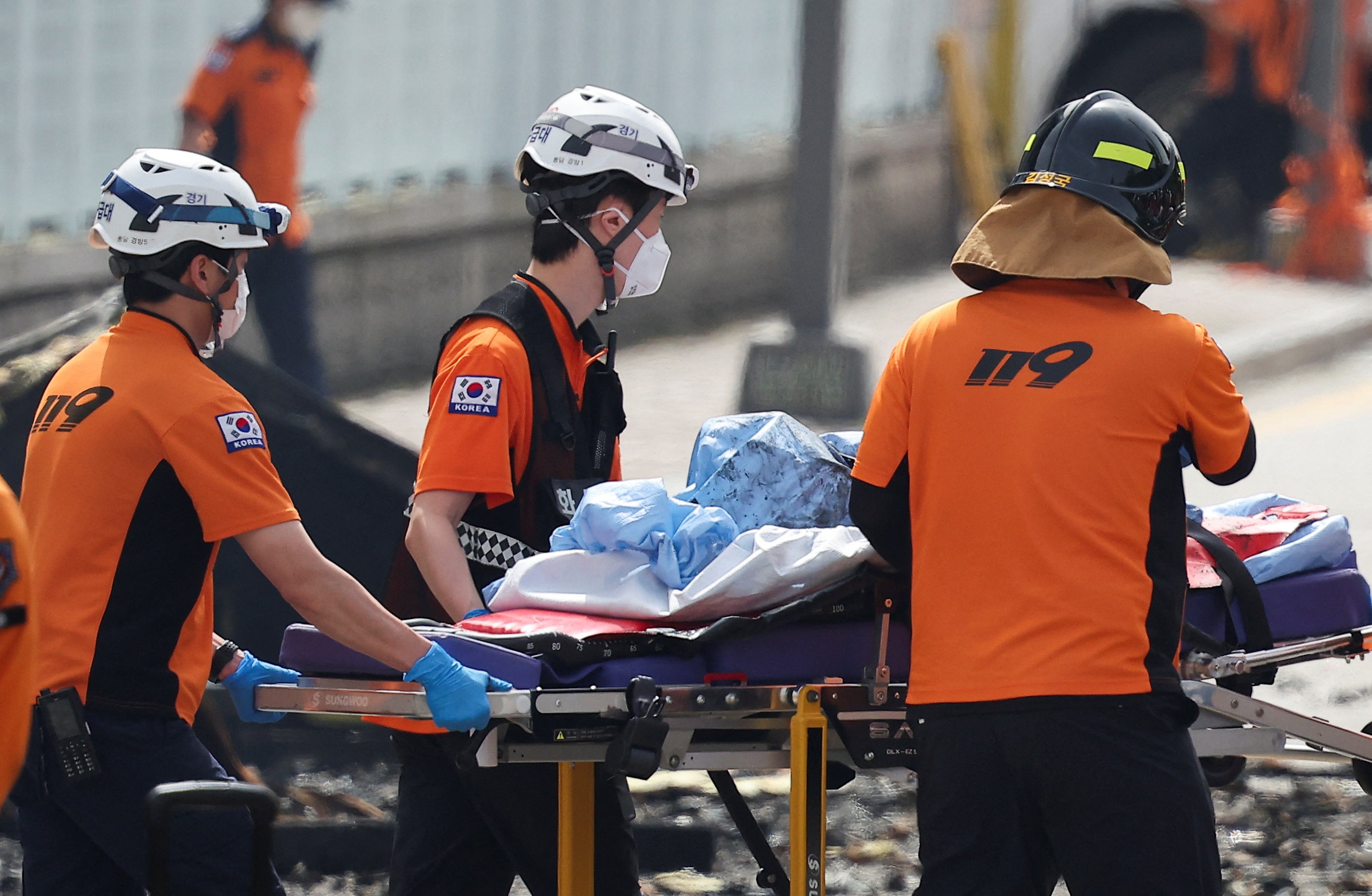 Emergency personnel carry the body of a person killed in a deadly fire at a lithium battery factory owned by South Korean battery maker Aricell