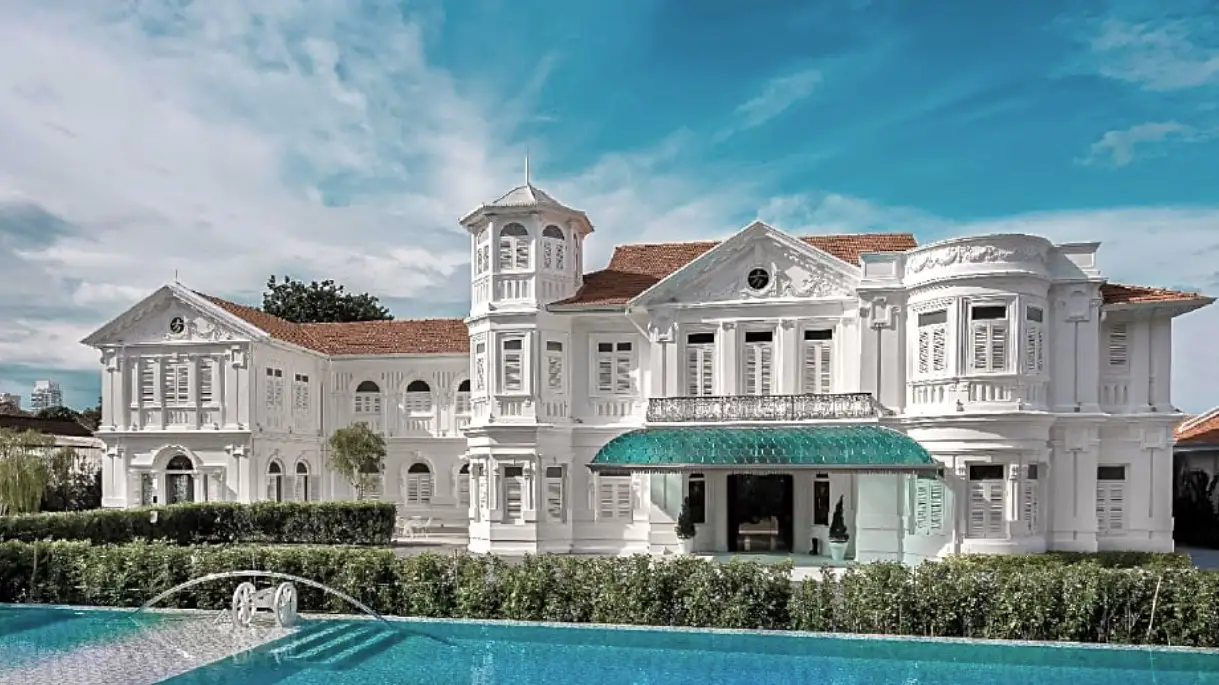 The Macalister Mansion, a beautifully restored colonial-era white mansion with intricate architectural details, set against a bright blue sky with a crystal-clear swimming pool in the foreground.