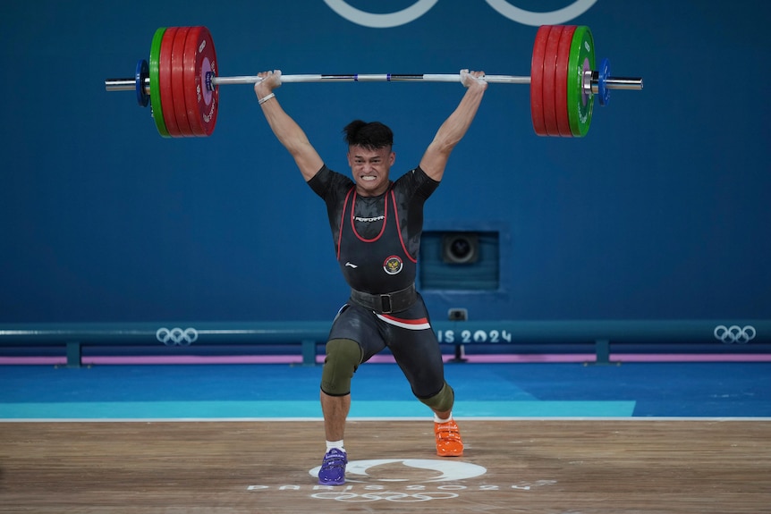 Rizki Juniansyah with weight above his head during weightlifting event at the 2024 Olympics.