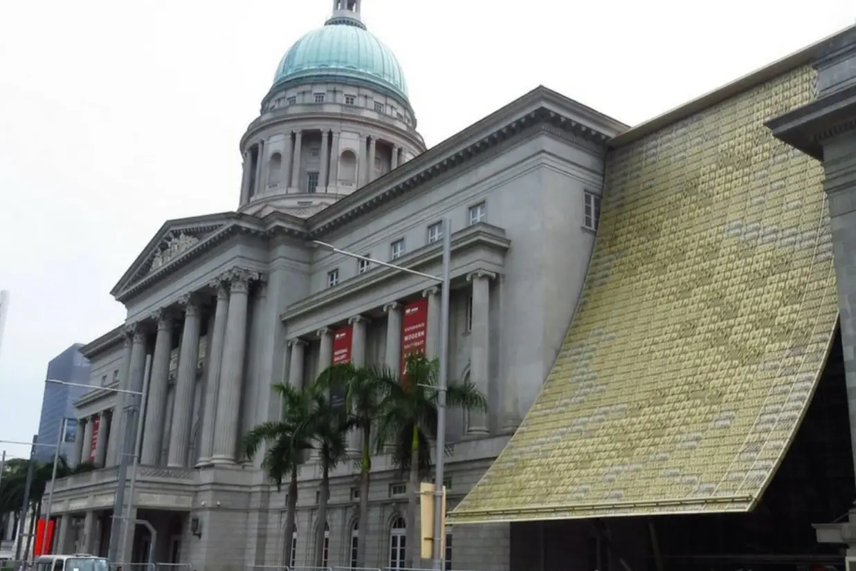 Exterior view of the National Gallery Singapore, featuring the neoclassical architecture of the former Supreme Court building with its large dome and the modern golden draped canopy.