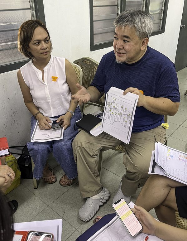 Jojo Ramos of Baguio City, Philippines, explains his artwork about what God means to him as his wife, Janet, watches.