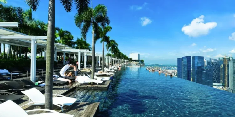 Infinity pool at Marina Bay Sands in Singapore, offering a stunning view of the city skyline and blue sky, with palm trees and lounge chairs lining the poolside.